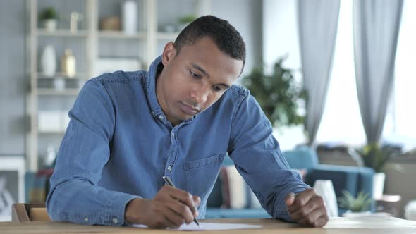 Young African Man Writing on Documents in Office, Paperwork