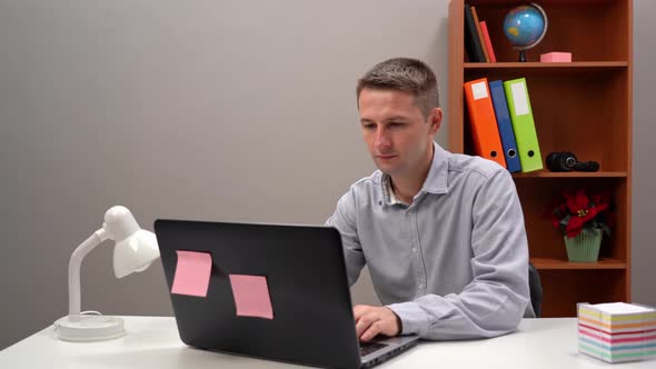 Young Guy Office Worker Manager is Typing Text in the Phone and in the Computer