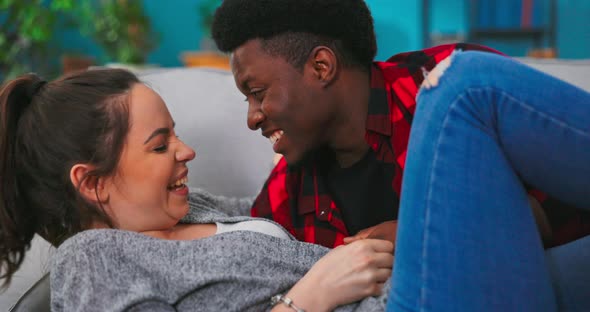 Close Up of the Cheerful Young Multiethnic Couple Lying on the Couch Hugging and Laughing