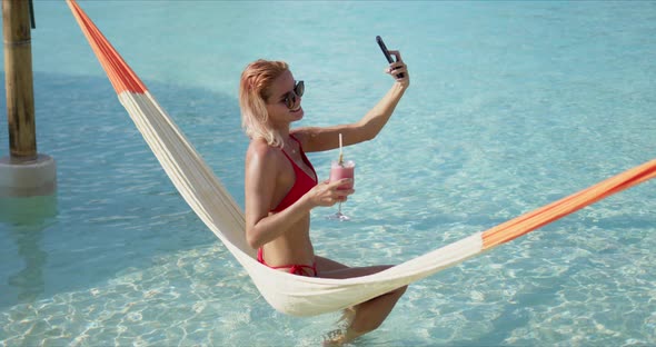 Female Tourist Drinking Cocktail and Taking Selfie on Hammock