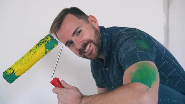 Builder Shows Roller with Yellow Paint Against White Wall