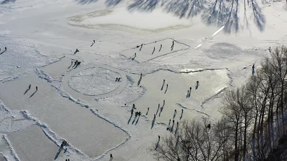 Aerial view of people on ice skating on frozen lake, skaters having fun on sunny winter day. Zlicin