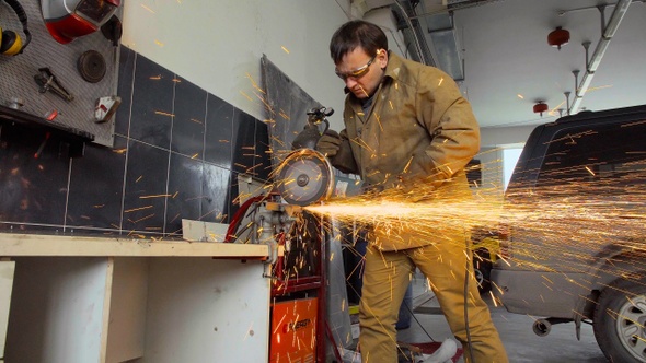 Worker using a grinder cuts metal in a workshop