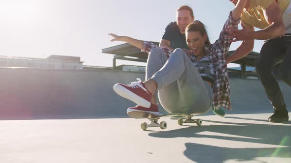 Laughing caucasian woman and two male friends, skateboarding on sunny day