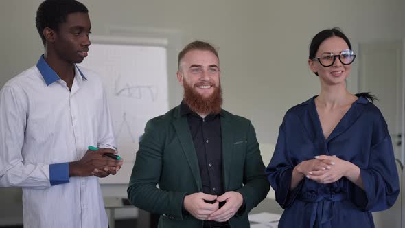 Smiling Bearded Businessman Talking Standing with Assistants in Board Room Indoors Looking Away