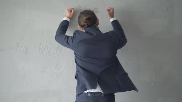 Back View of Furious Irritated Angry Man Beating Grey Wall. Middle Shot of Aggressive Caucasian