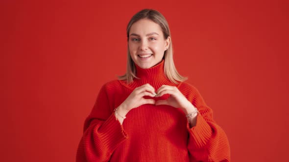 Lovely woman wearing red sweater showing heart shape gesture