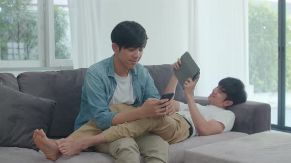 Young gay lgbtq couple using mobile phone and tablet at modern home