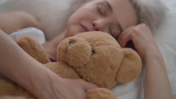 Closeup Teddy Bear with Blurred Mature Woman Sleeping in Bed at Background