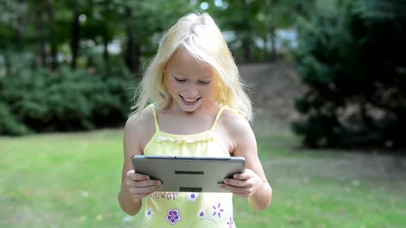 Little Smiling Girl Plays the Game on the Tablet in the Park - She Rotates the Tablet