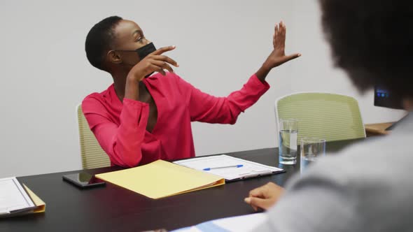 African american businesswoman in face mask pointing to screen and talking to colleagues at meeting