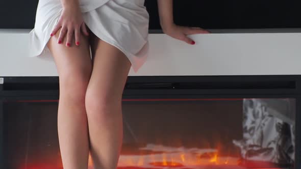 Beautiful Legs of a Girl on the Background of a Decorative Fireplace in the Room. Girl Spiral on the