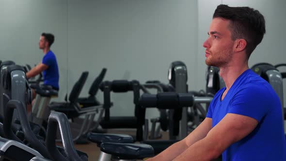 A Young Fit Man Trains on an Exercise Bike in a Gym - Closeup From the Side