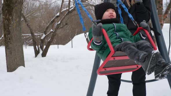 Mom Entertains the Baby on a Winter Swing