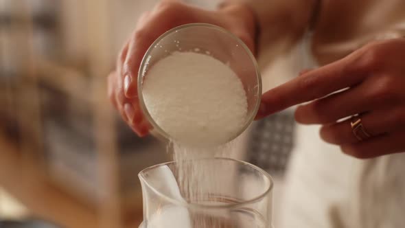 Closeup Hands of Unrecognizable Female Artisan Pouring Dry Ingredient Into Glass Measuring Jar for