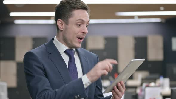 Businessman Celebrating Success on Tablet in Office