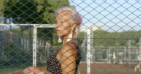 Blond Woman Turns Around at Stadium Grid Against Green Trees