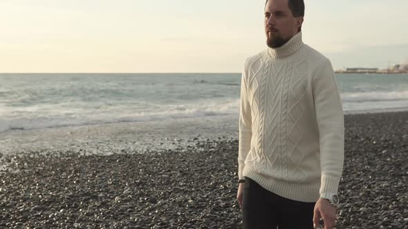 Thoughtful Young Man Is Strolling on Sea Shore in Autumn Sunny Evening