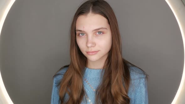 A Beautiful Young Girl with Blue Eyes in a Blue Sweater Poses in Front of the Camera
