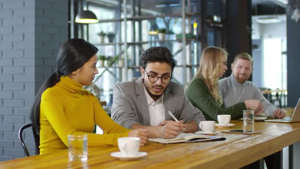 Arab Businessman Speaking with Asian Colleague at Restaurant Table