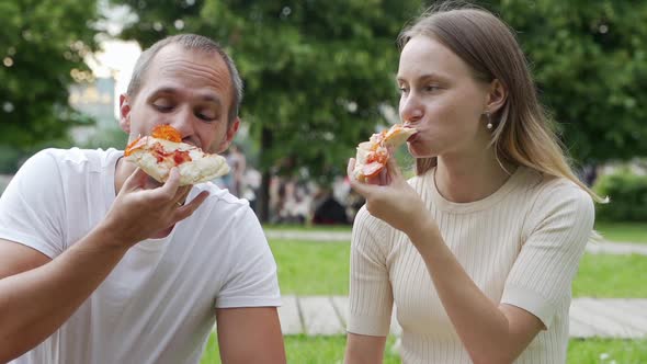 Young Couple Eating Pizza Outside. Woman and Man Having Picnic in Park. Fast Food Concept.