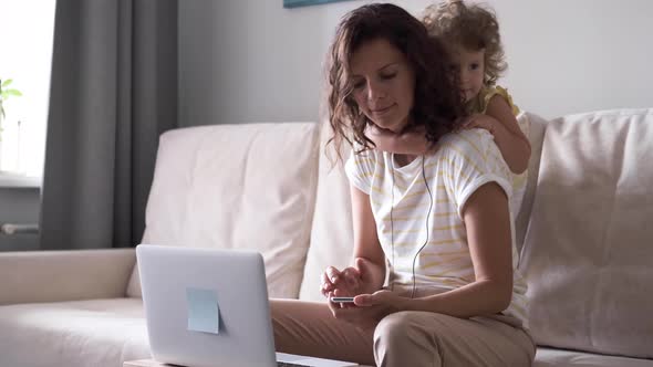 Mother Multitasking Using Laptop Computer at Home with Her Baby. Candide Genuine and Real Life Mom