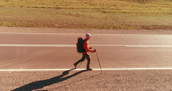 Flight Over Hitchhiker Tourist Walking on Asphalt Road. Huge Rural Valley at Summer Day. Backpack