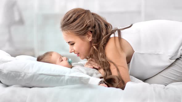 Happy Caring Mother Playing with Cute Toddler Lying on Bed Enjoying Morning Together