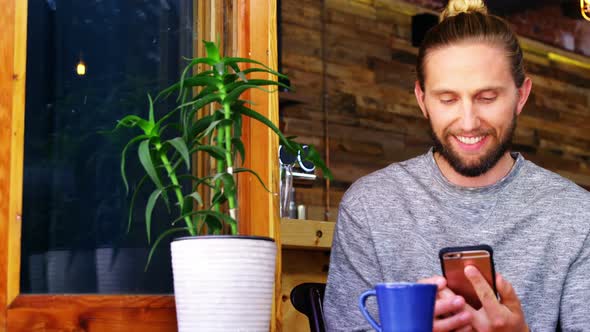 Handsome man using mobile phone while having coffee