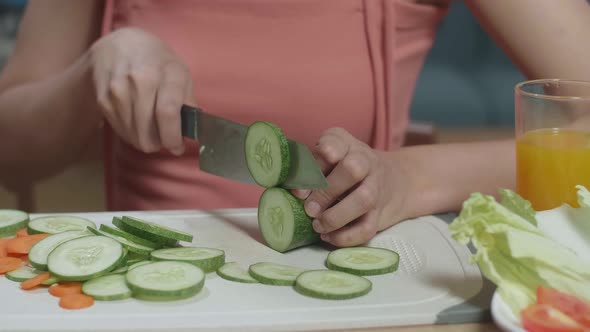 Close Up Of Asian Woman Holding A Knife And Slicing Cucumber On The Chopping Board In The Kitchen