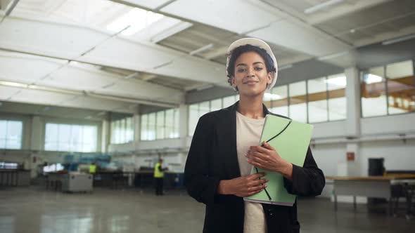 Portrait of African American Happy Woman in Helmet and Suit Holding Documents and Presenting