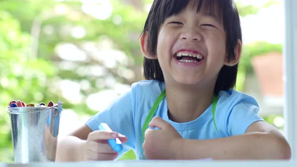 Cute Asian Child Drawing With Crayons On White Table