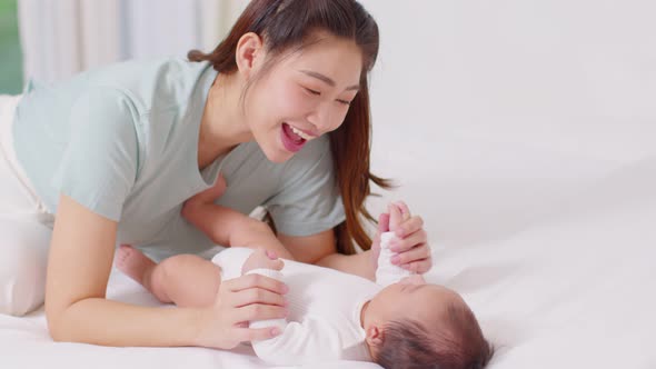 New asian mom playing to adorable newborn baby on bed smiling and happiness at home