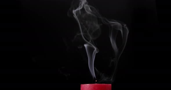 Red candle burning on black background. Blow out the candle. Smoke goes up. Close-up