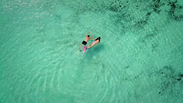 Aerial view of man and woman swimming in masks and flippers in turquoise water.