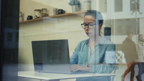 A Lady in Glasses Working with a Computer Seen Through the Window