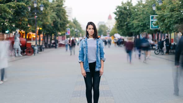 Zoom in Time-lapse of Pretty Girl in Trendy Clothing Looking at Camera Standing on Pedestrian Street