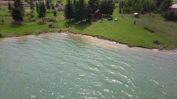 Aerial Panning Shot of edge of lake with a cabin in the background