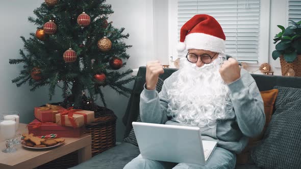 A Cheerful Man in a Santa Claus Costume in a Santa Hat Beard and Glasses Cheerfully Communicates