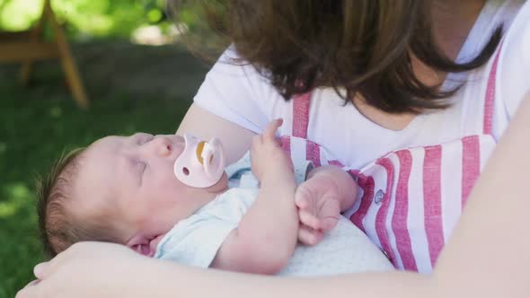 Mother with a Newborn Baby Walks in the Park. Young Mother Holds Her Baby in Her Arms. Breast