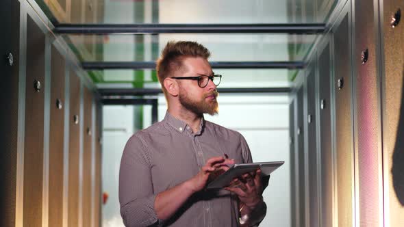 Computer Engineer Works with Tablet While Checking Computers at Data Center.