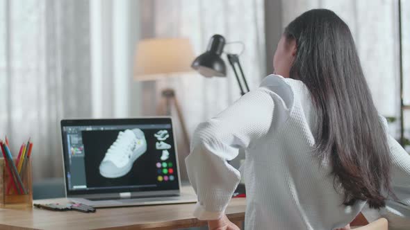 Asian Female Footwear Designer Having A Backache While Designing Shoe On A Laptop At Home