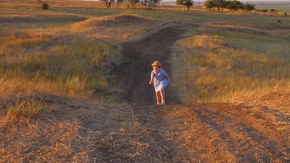 Adorable little girl in blue summer dress climbing up the hill. Child running in wild grass country