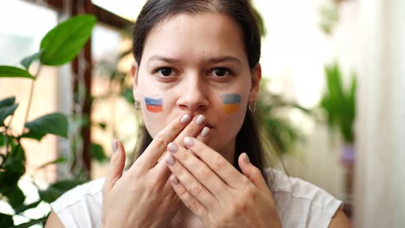 Young RussianUkrainian Girl with the Flag of Ukraine and Russia on Her Face is Closing Mouth