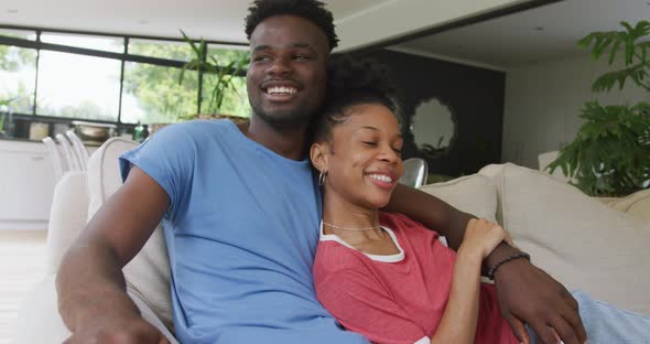 Video of happy african american couple sitting on sofa and embracing