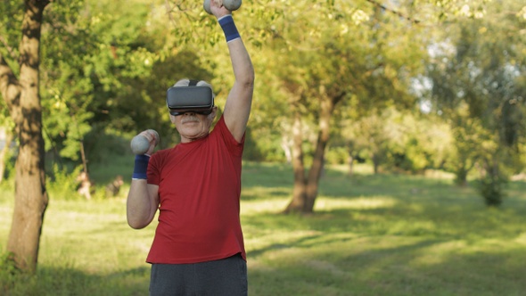 Senior Old Grandfather Man in VR Headset Helmet Making Fitness Exercises with Dumbbells in Park