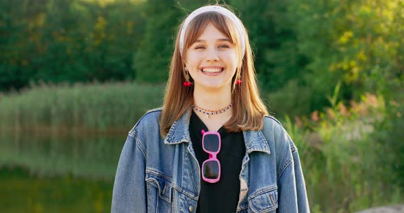 Portrait of a Cheerful Teenage Girl with a Bandana on Her Head Standing in a Forest Near a Lake