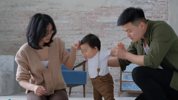 First step. Loving young parents hold hands of an innocent baby inside the room