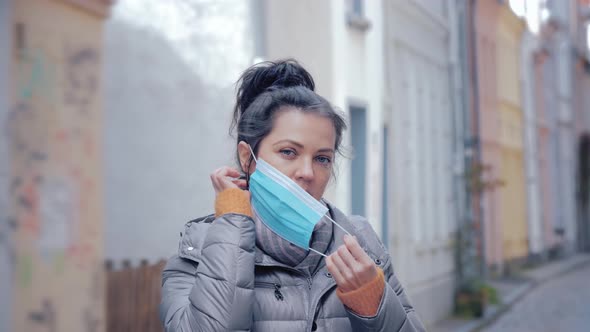 Woman in City Street Putting on Face Protective Mask