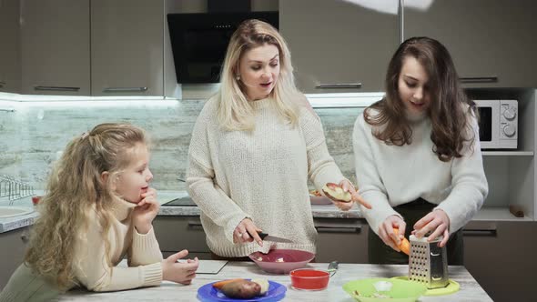 Young Mother and Two Her Daughters Cooks Salad at Kitchen